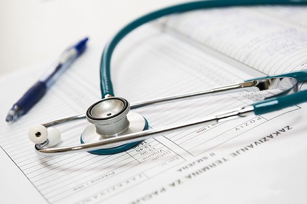 Blue stethoscope and blue pen laying on top of a time tracker notebook